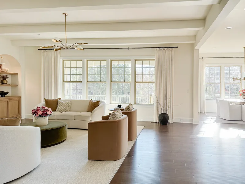 The seating group from the far corner, beamed ceiling and brass chandelier above sunlit wood floors