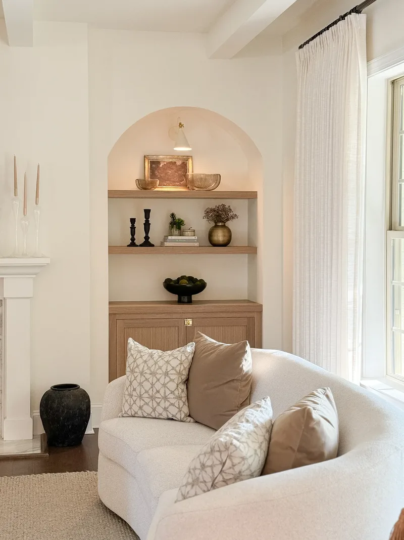 Looking into the arched niche past the curved sofa's pillows, sheer curtains at the tall window