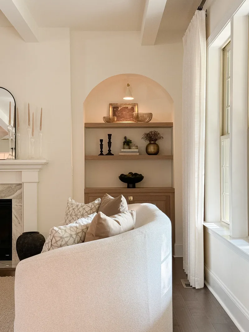 The niche seen over the back of the sofa, window wall and pinch-pleat curtain at right