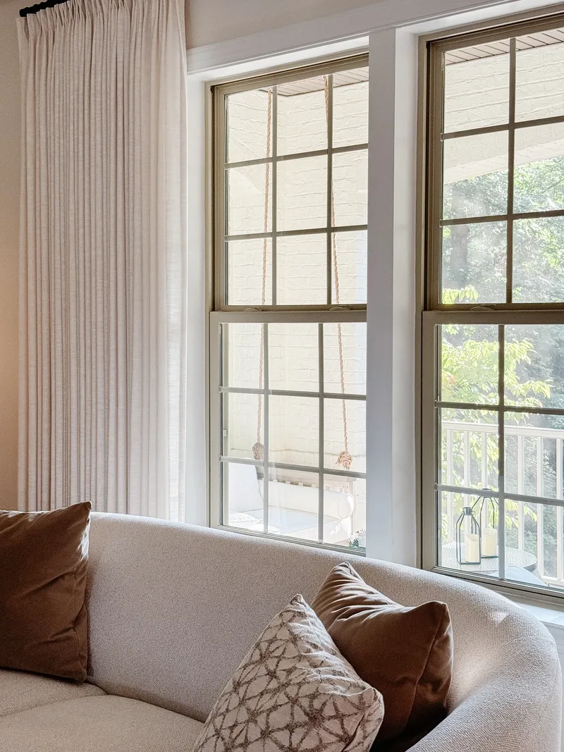 Two grid windows with rope sash pulls looking onto a screened porch, sofa pillows below