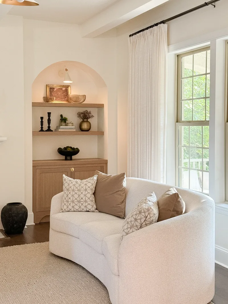 A curved bouclé sofa set in front of the niche, jute rug underfoot, daylight from the right