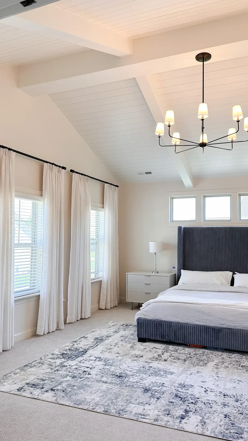 Vaulted plank ceiling and black chandelier above a navy channel-tufted bed and fluted white nightstand