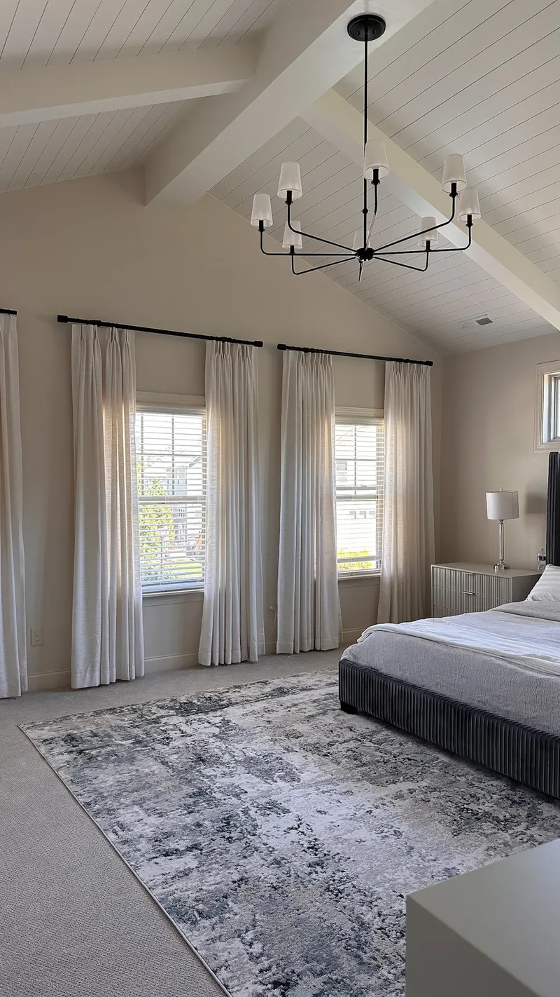 A blue-grey abstract rug runs from the curtained windows to the foot of the navy bed