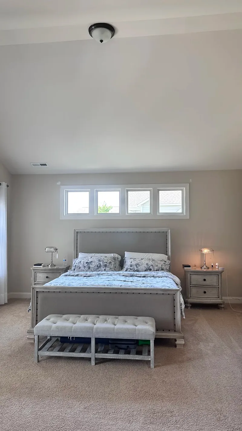 The bedroom before the remodel, with a grey nailhead bed and matching nightstands under a plain domed light