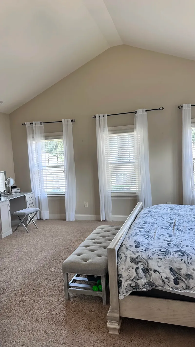 Before the remodel again, seen from the bed's foot: sheer curtains, blinds and a small white vanity