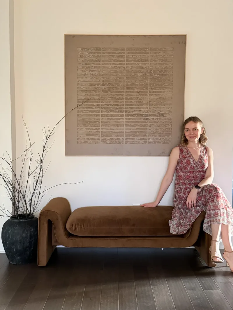 Tatyana perched on the arm of the caramel velvet bench beneath the textured canvas in the entry