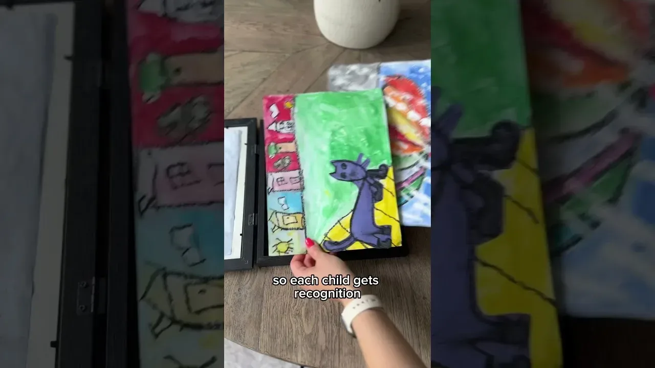 Video still: children's paintings being slipped into a black storage frame