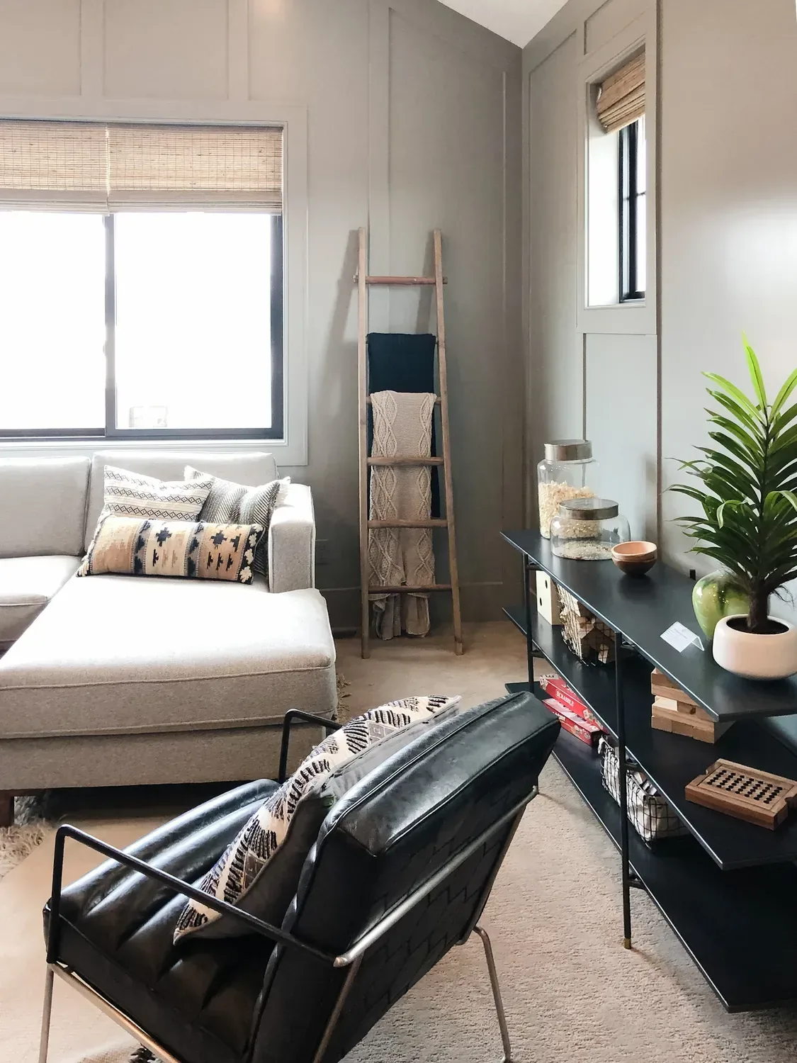 A living room wall in grey board-and-batten panelling behind a blanket ladder and black console