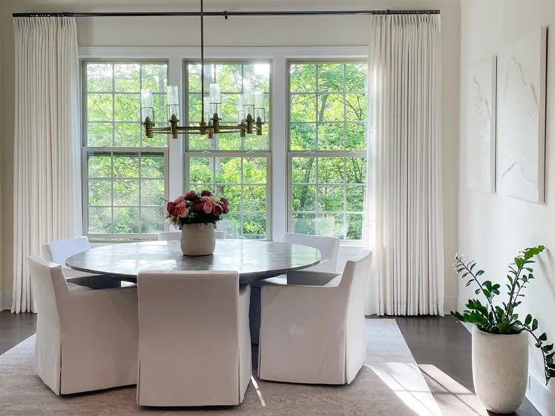 The dining table straight on, roses in a stone vase, brass chandelier centred between three tall windows