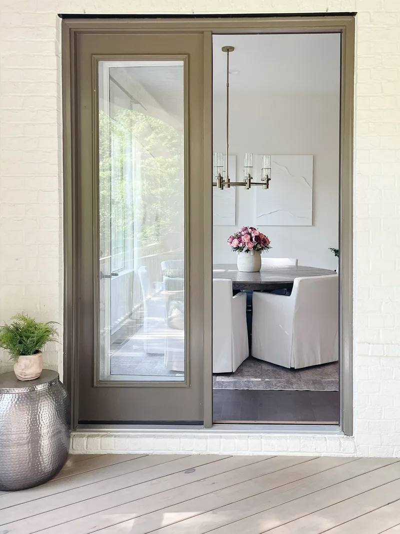 The dining room glimpsed through an open door from the painted-brick porch, roses on the table