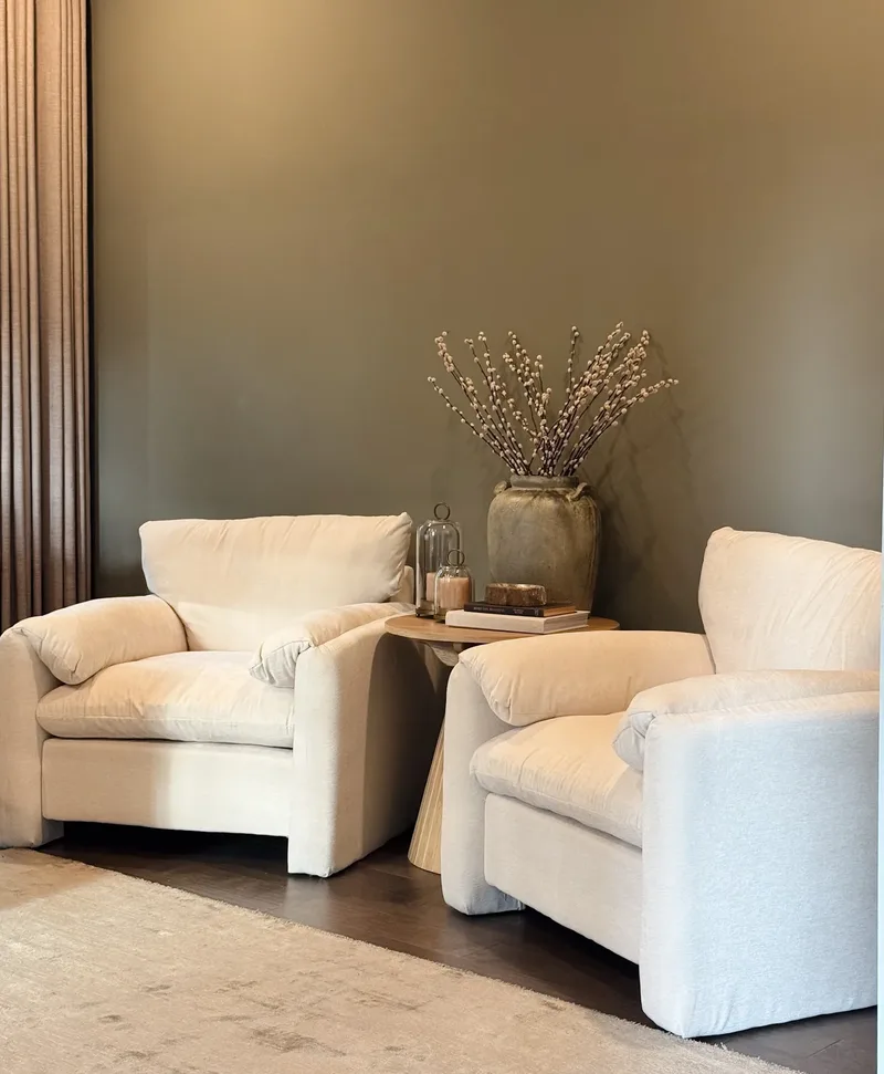 Deep cream armchairs facing each other across a round wooden table with candles and pussy willow branches
