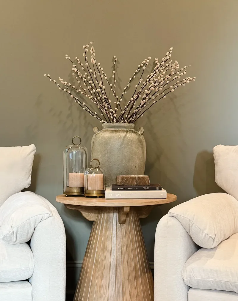 On the table between the chairs: a stone urn of pussy willow, candles under glass cloches, books