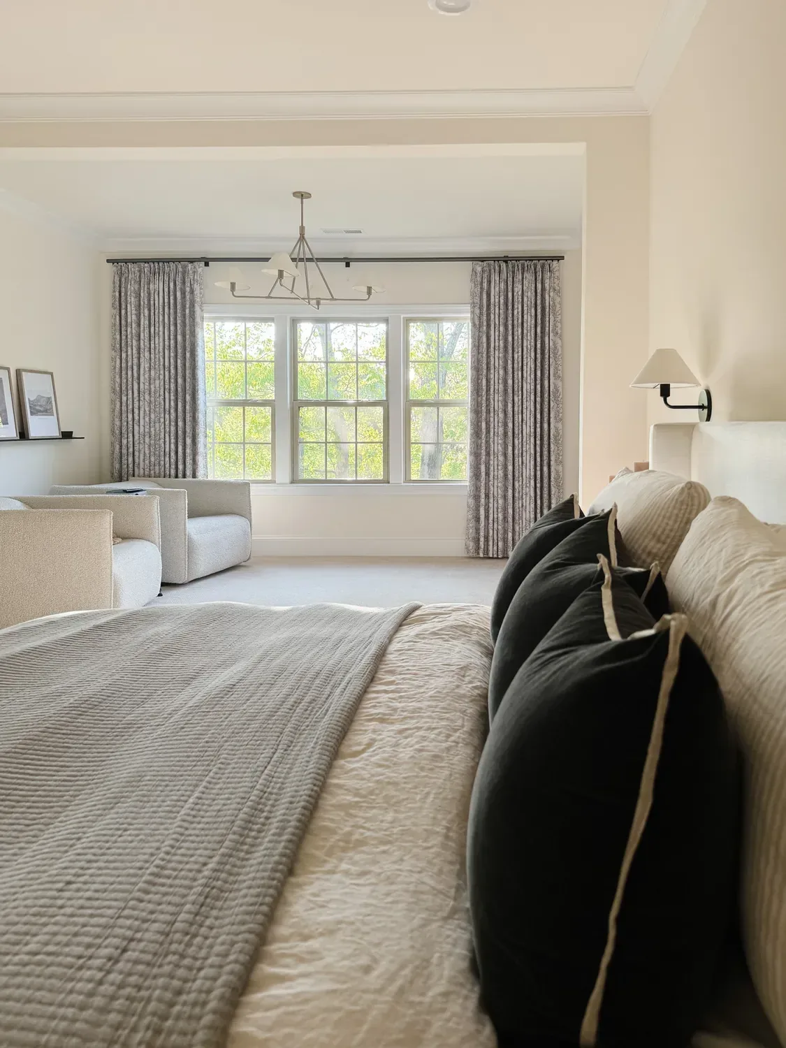 Floral pinch pleat drapes framing the master bedroom windows, boucle chairs below