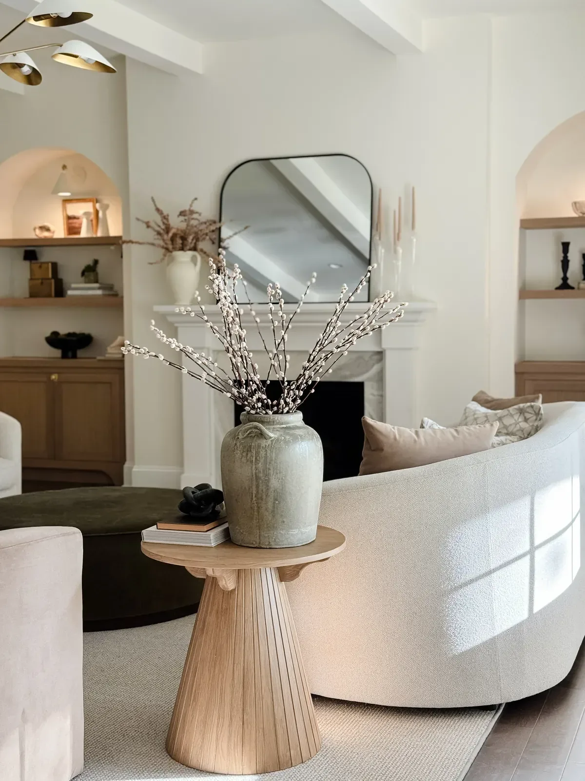 Living room with a curved bouclé sofa, fluted side table and an arched mirror over the mantel