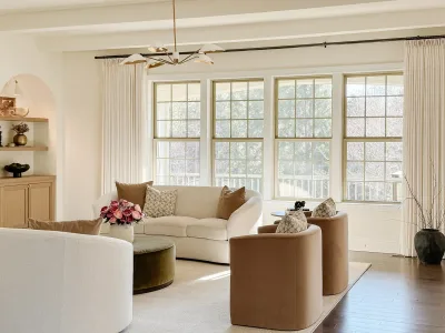Living room with a cream sofa, tan swivel chairs and tall windows onto the deck